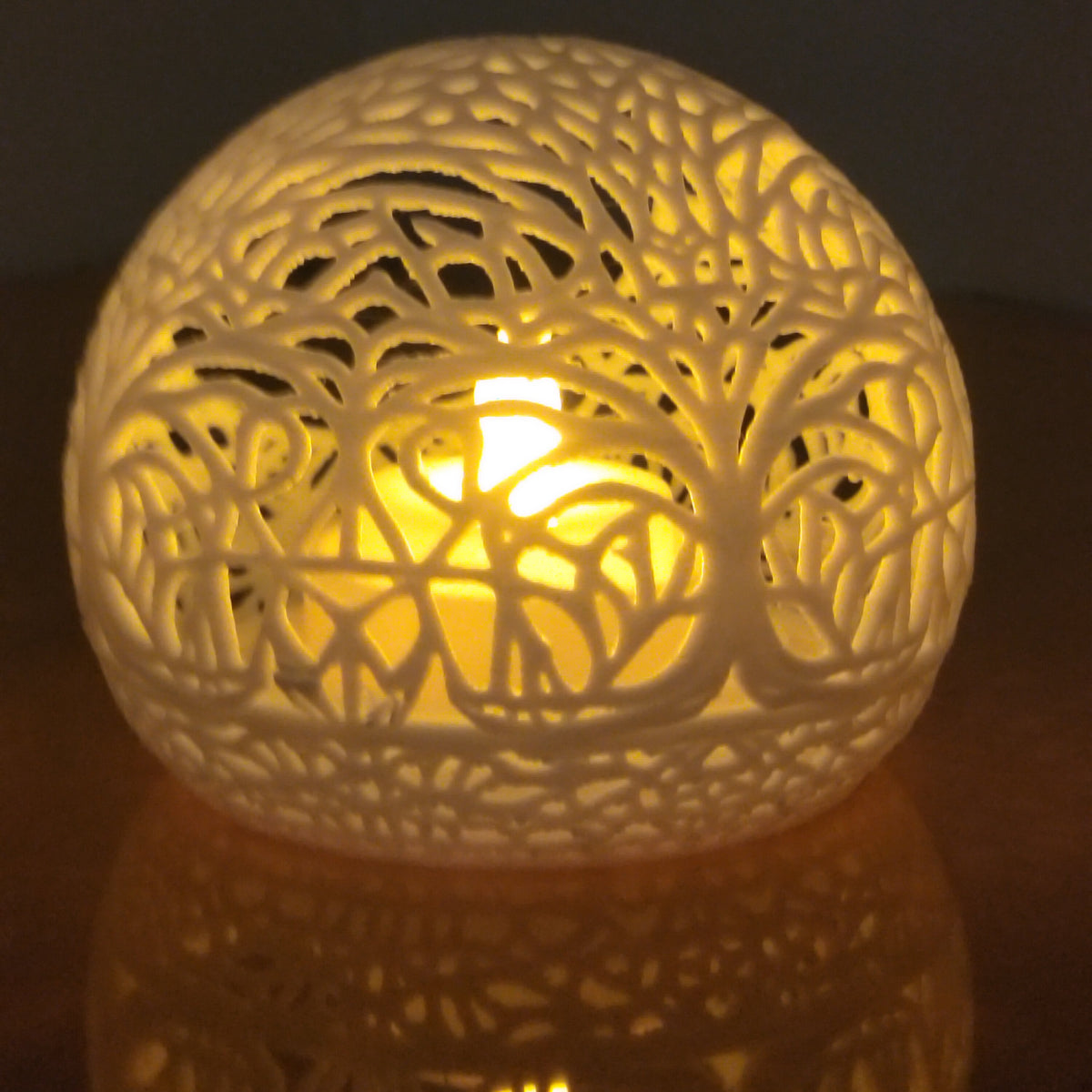 A spherical decorative lamp with an intricate tree branch cutout pattern, glowing warmly from a central light source against a dark background.