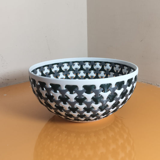 A fruit bowl with a black , dark green and white geometric star pattern, sitting on a glossy orange table against a beige wall.