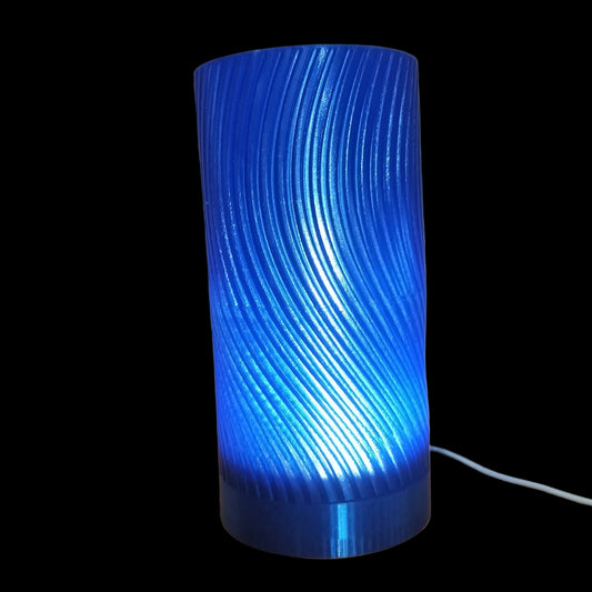 A blue cylindrical table lamp with a ribbed, wavy-textured glass shade, glowing with a bright blue light