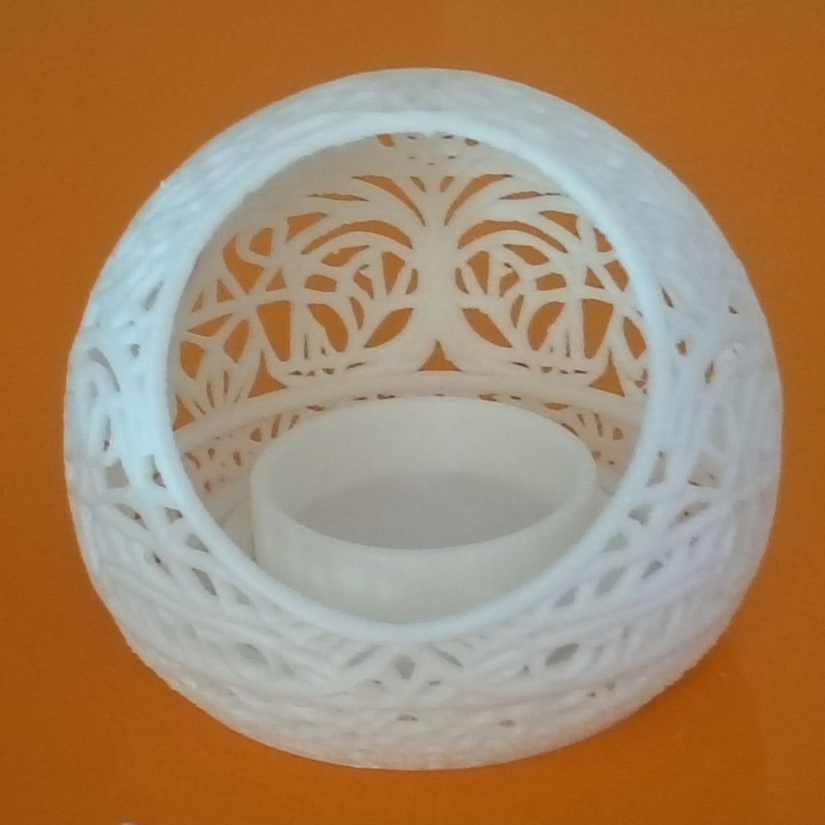 A white 3D-printed spherical candle holder with intricate laser-cut tree of life patterns, shown on a bright orange background.
