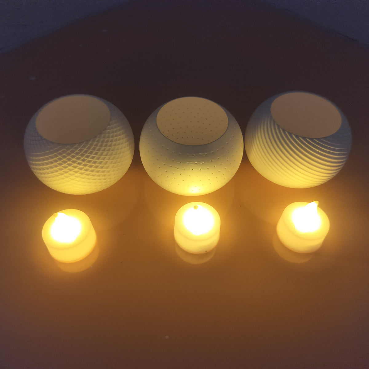 Three textured glass candle holders with matching lit tealight candles, arranged on a dark brown surface.
