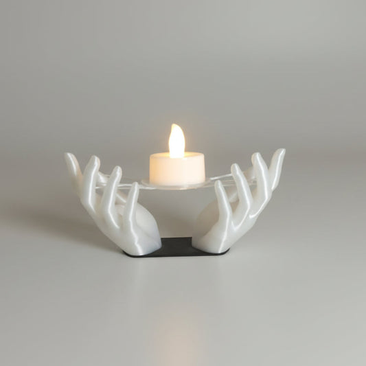 A white sculptural candle holder shaped like branching arms, holding a small lit candle on a glossy mustard-yellow tabletop against a plain off-white wall.