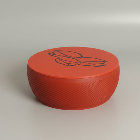 A round red storage box with a black line-art illustration of cocoa beans on top, resting on a yellow surface in the corner of a room.