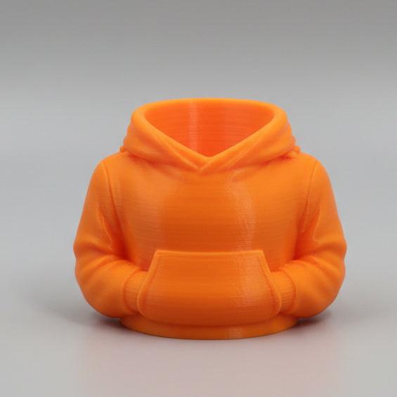 An orange 3D-printed miniature hoodie pen holder with a front pouch pocket, set against a neutral gray studio background.