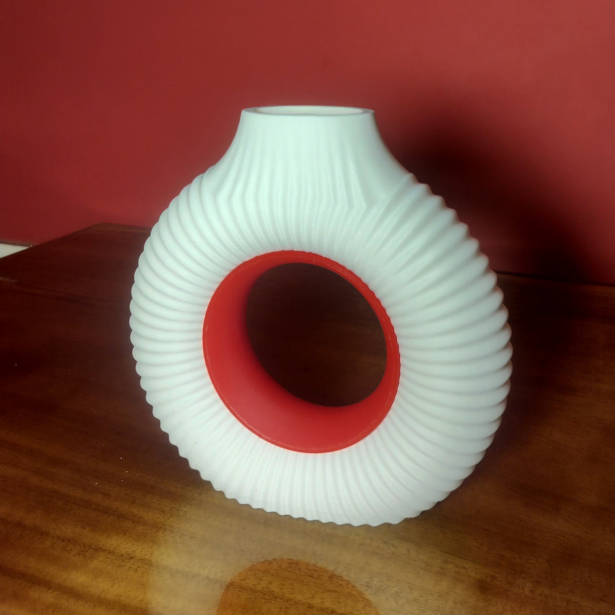 A white ribbed silicone personal massager with a red inner ring, standing on a wooden surface against a solid red background.